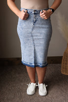 Person wearing a denim skirt and white sneakers indoors.