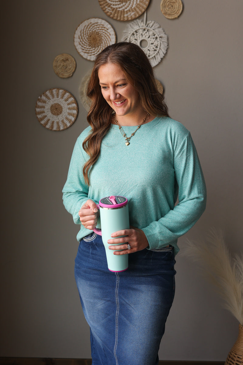 ash teal soft long sleeve top and denim skirt on a woman standing against a neutral wall