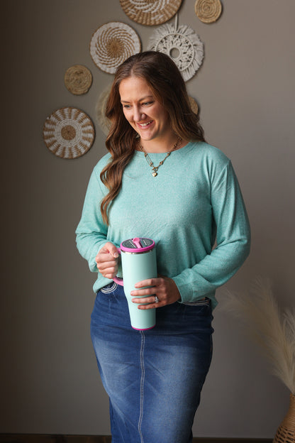 ash teal soft long sleeve top and denim skirt on a woman standing against a neutral wall
