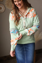 Woman wearing a light green blouse with floral patterns and blue jean skirt indoors.