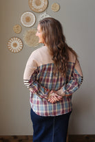 A woman with long brown hair is shown from behind wearing a color-blocked plaid top. The top features a beige yoke, tan sleeves, and a blue, red, and beige plaid body.