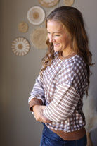 Side view of a brown and cream plaid top showing its striped sleeve and gathered wrist cuff.