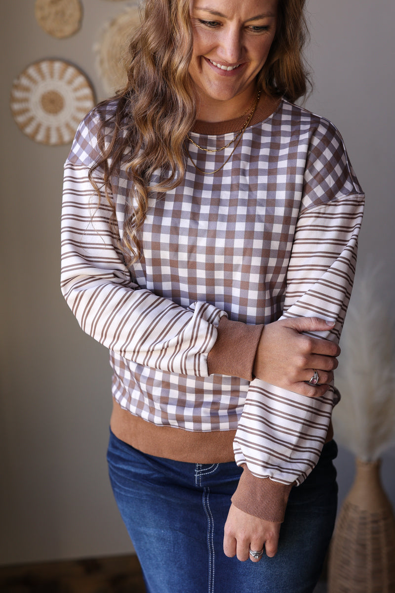 Close-up of a brown and cream gingham top with contrasting striped long sleeves and gathered cuffs.