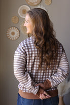 Angled back view of a brown and cream plaid top with contrasting striped long sleeves.