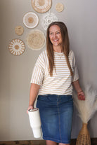 Woman wearing a beige white striped half sleeve top for casual spring office outfits, in front of decorative wall art.
