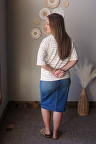 Woman wearing a striped shirt and blue skirt standing in a room with decorative wall art.
