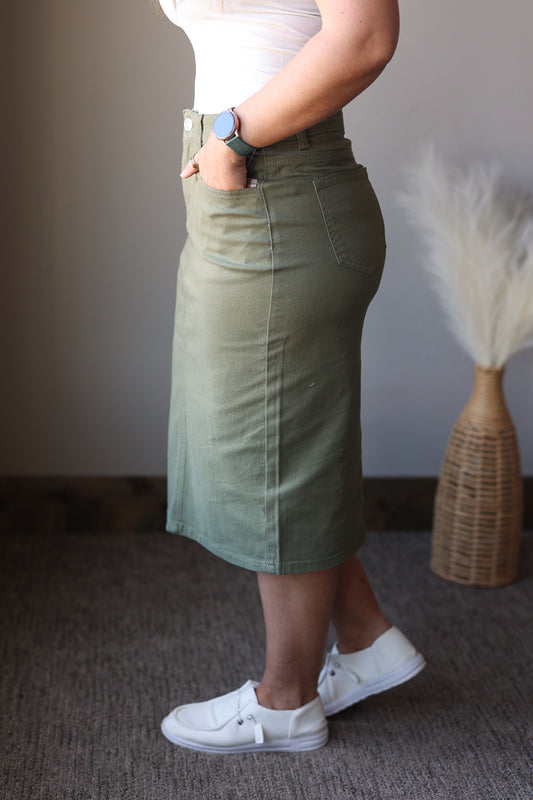 Person wearing a green skirt and white sneakers in a minimal indoor setting