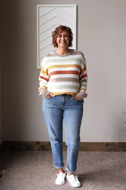 Person wearing a striped sweater and jeans standing indoors.