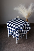 Black and white checkered blanket draped over a chair with a decorative vase of pampas grass on a plain background