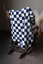 Checkered blue and white blanket draped over a wooden chair against a neutral background
