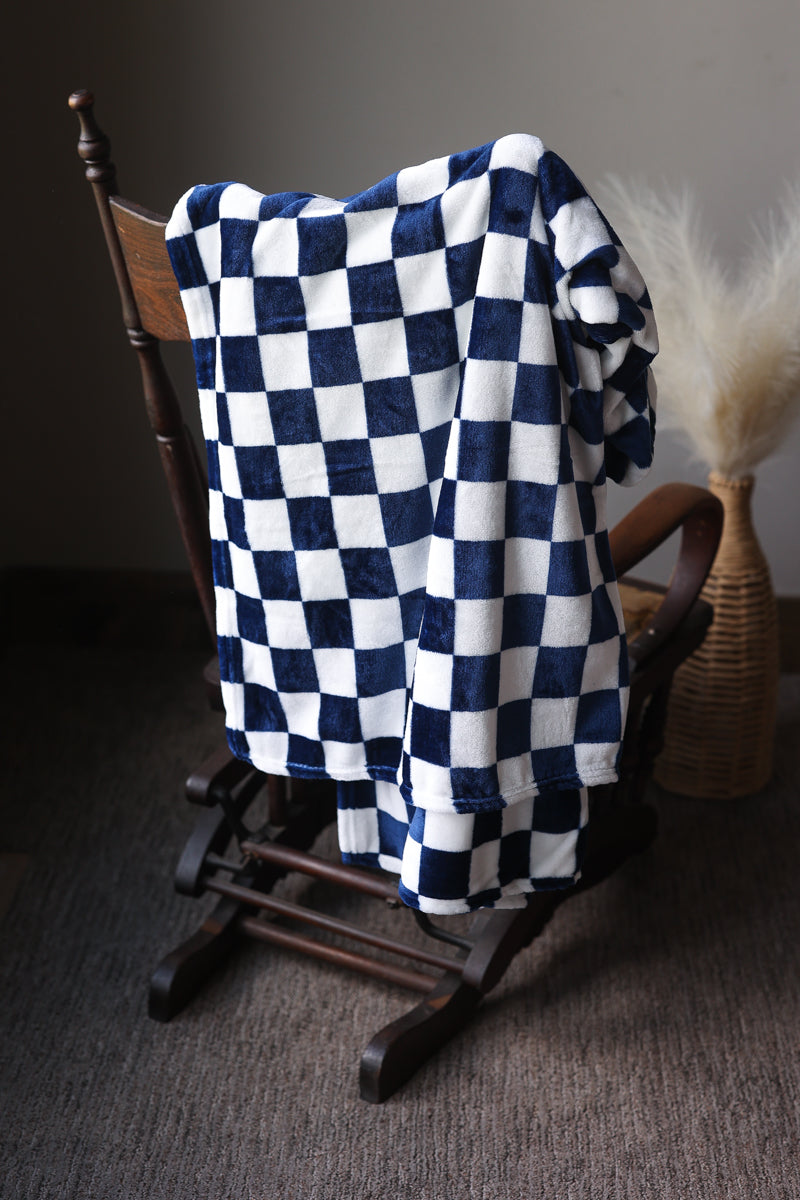 Checkered blue and white blanket draped over a wooden chair against a neutral background