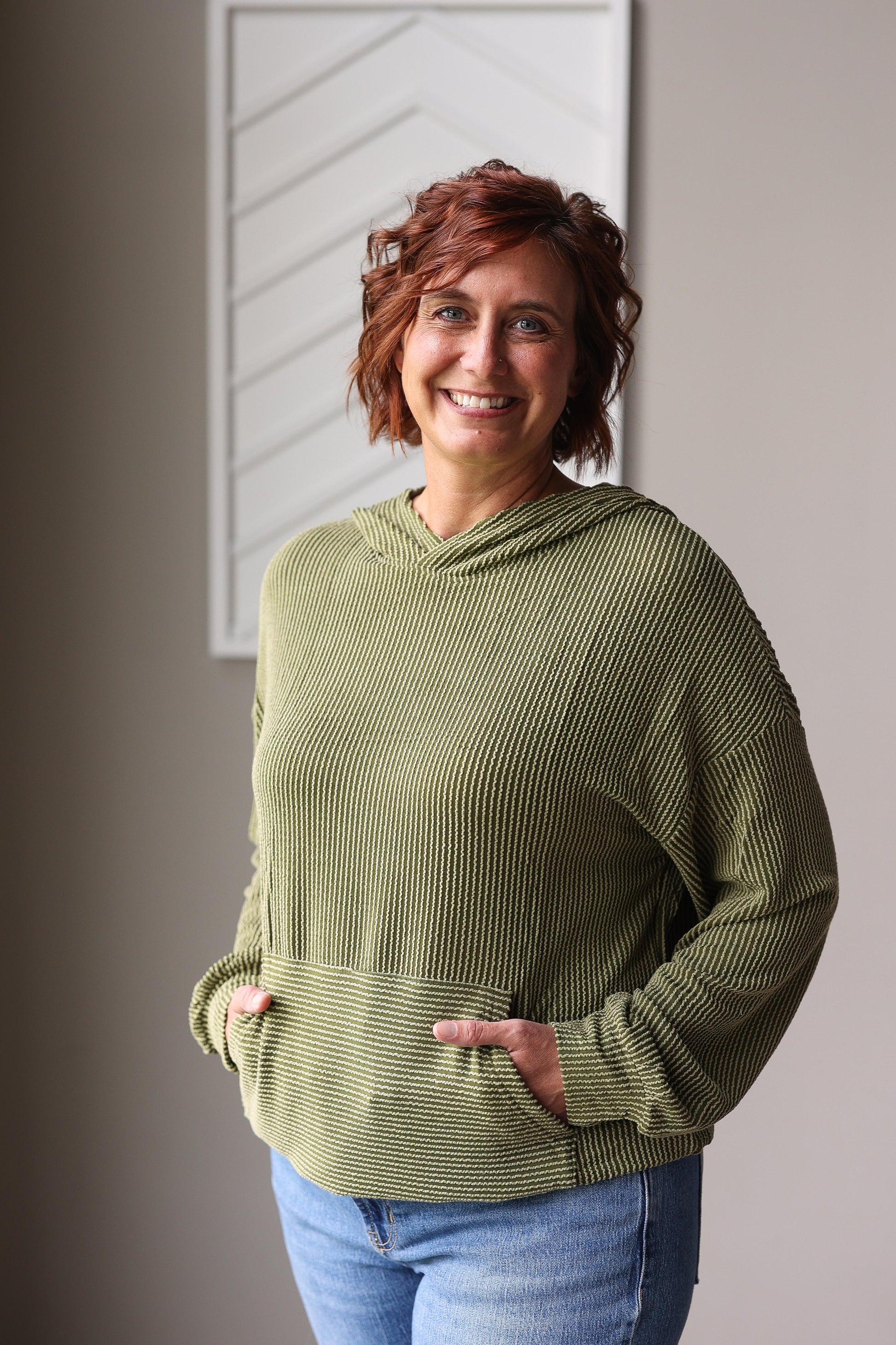 Woman wearing a green textured sweater standing indoors against a neutral wall.
