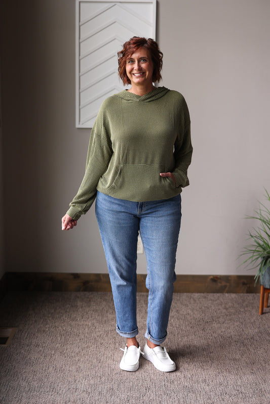 Woman wearing a green sweater and blue jeans standing indoors from Classy Closet