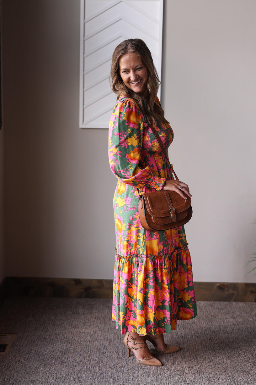 Woman wearing a colorful floral dress holding a brown leather bag indoors.