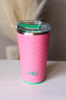 Pink swig tumbler with a green lid on a pink golf dimple surface SWIG