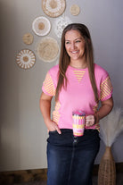 Woman in a pink shirt holding a colorful cup against a wall with decorative plates.