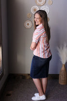 Woman wearing a striped shirt and denim skirt standing in a room with decorative wall art.