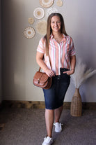 Woman in a striped shirt and skirt holding a brown bag, standing in a room with decorative elements.