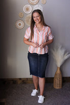 Woman wearing a striped shirt and denim skirt standing in a room with decorative wall art.