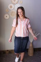 Woman wearing a striped shirt and denim skirt standing in a room with decorative wall art.