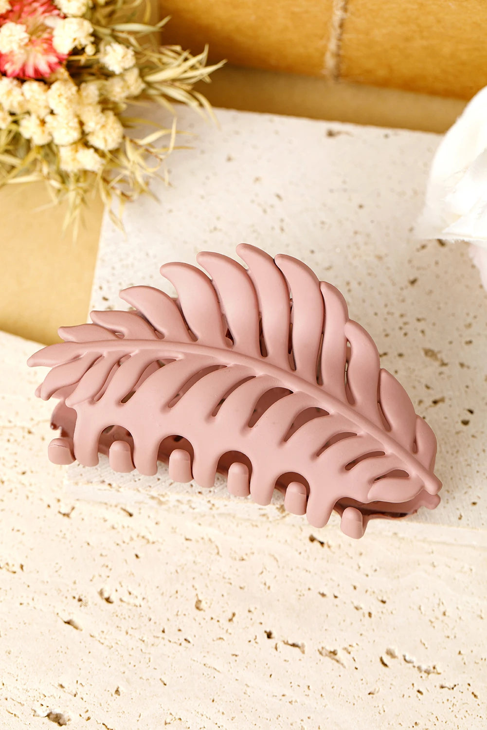 Pink leaf-shaped hair clip on a textured surface with flowers in the background