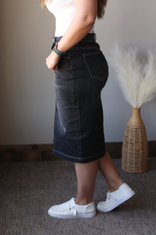 Person wearing a black denim skirt with white sneakers in a room setting.