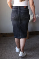 Person wearing a black denim skirt with a plain background