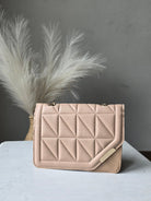 A light beige quilted leather clutch bag with a geometric diamond pattern, displayed on a white surface next to a white decorative feather.