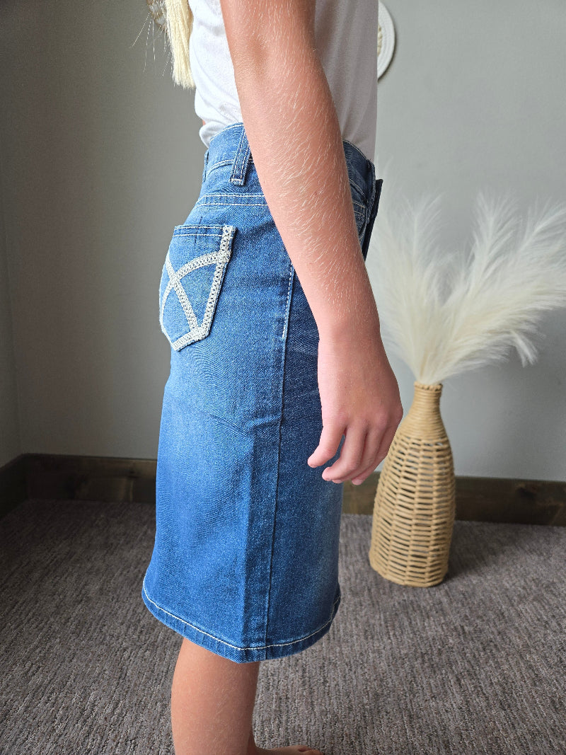 A child wearing a blue denim skirt with white embroidered details, shown from the side in an indoor setting.