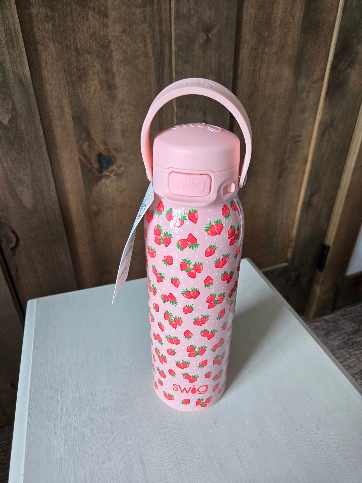 Pink water bottle with strawberry pattern on a wooden surface
