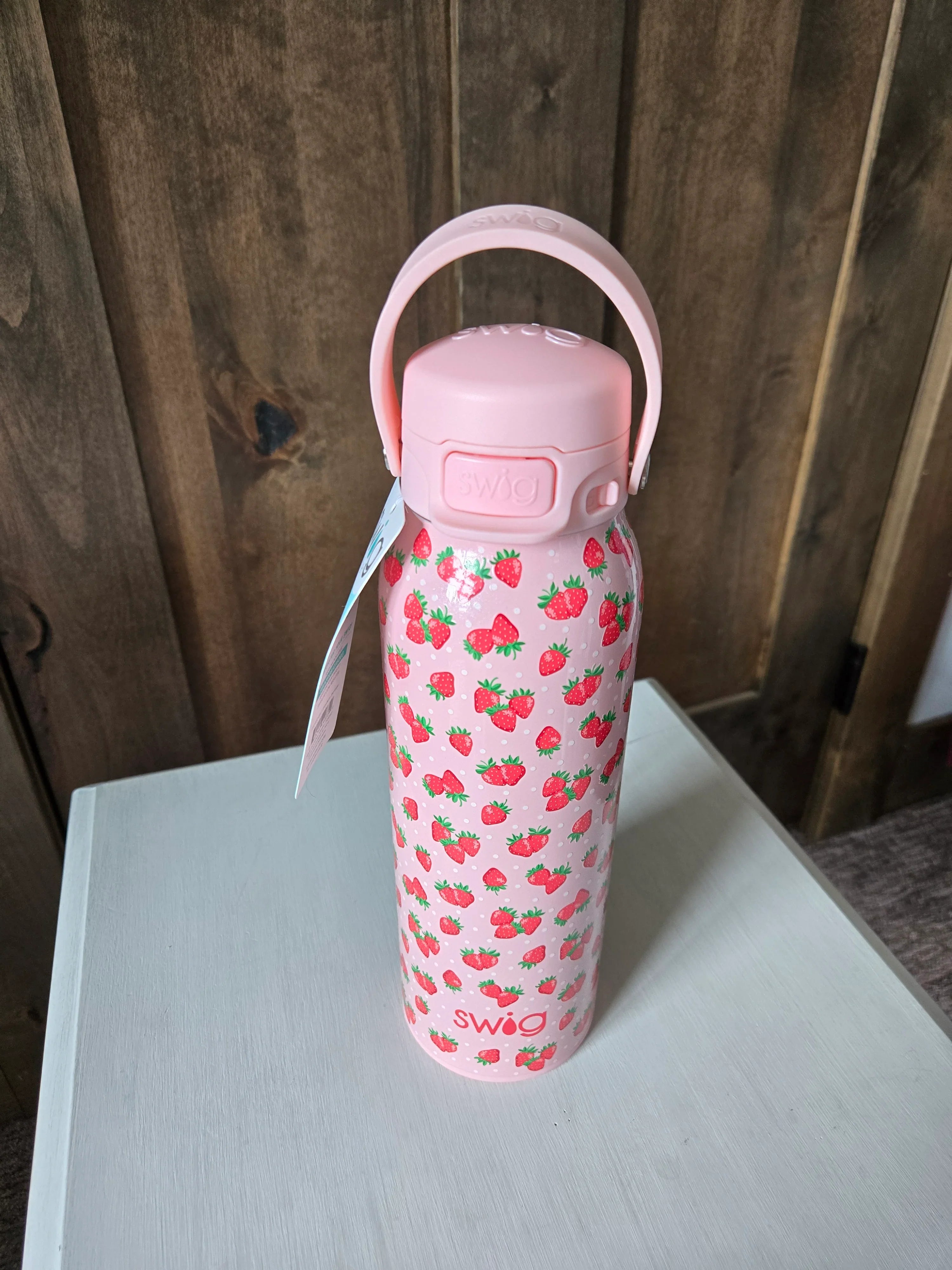 Pink water bottle with strawberry pattern on a wooden surface