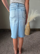 A person wearing light-wash denim shorts, shown from the back in a home setting with a woven vase on a neutral surface.