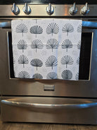 A white kitchen towel with a black palm fan pattern hanging on the oven door of a stainless steel range.