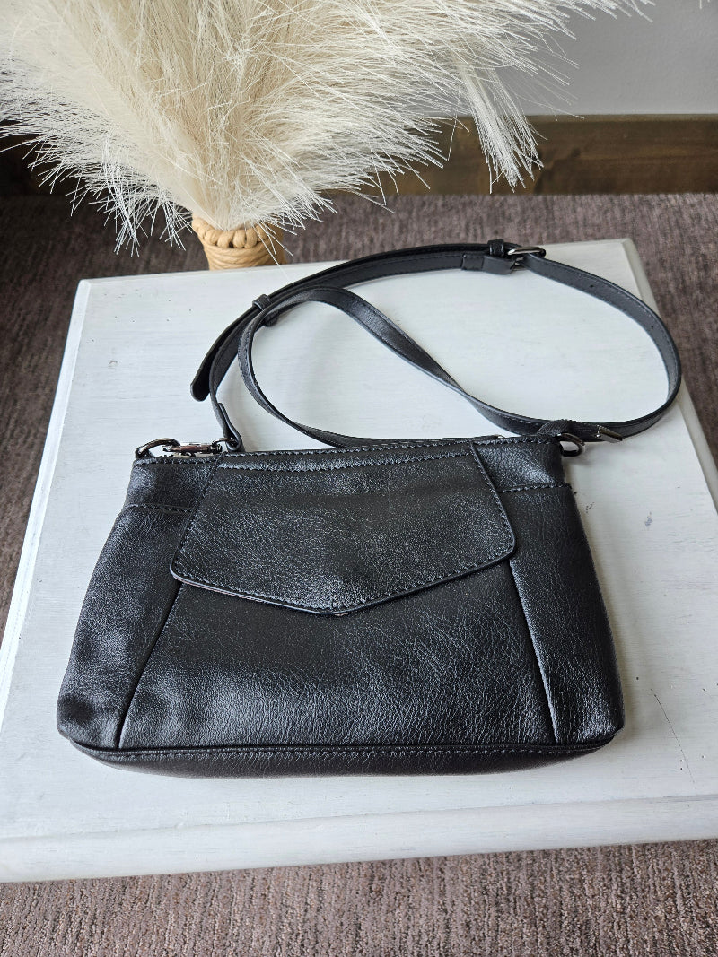 Black leather crossbody handbag with a flap front pocket and adjustable shoulder strap, displayed on a white rectangular surface with dried pampas grass in the background.