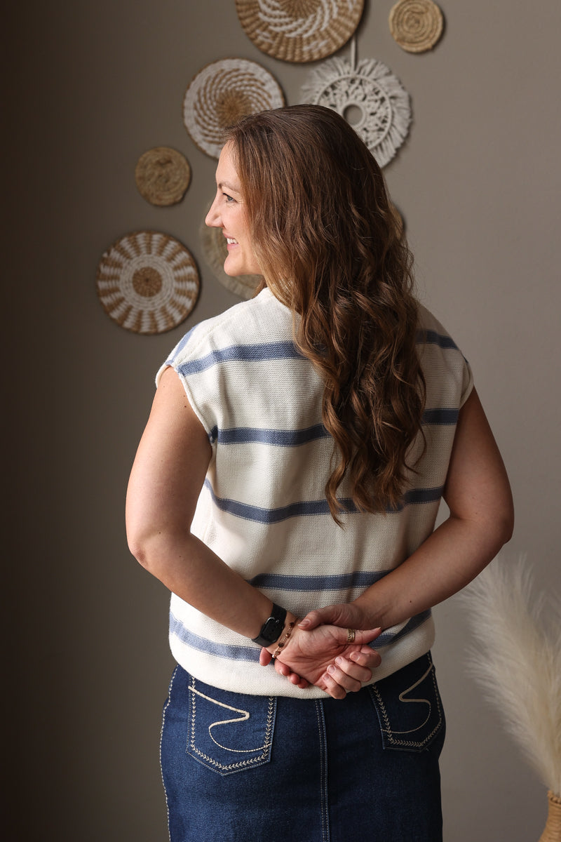 Woman wearing a striped shirt and blue jean skirt standing against a wall with decorative plates.