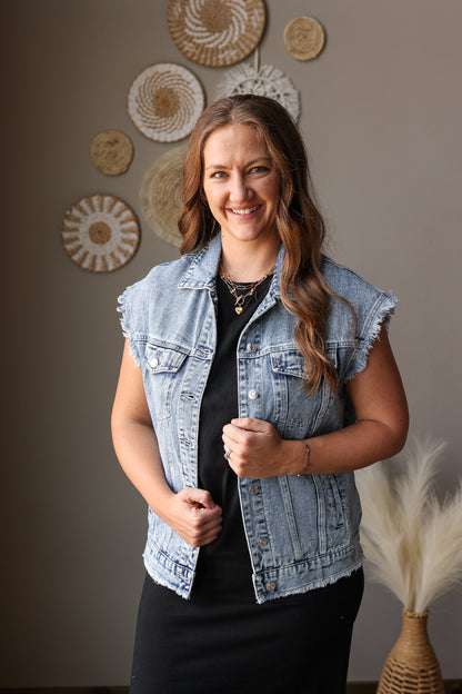 Woman wearing a denim vest standing in front of decorative wall art.