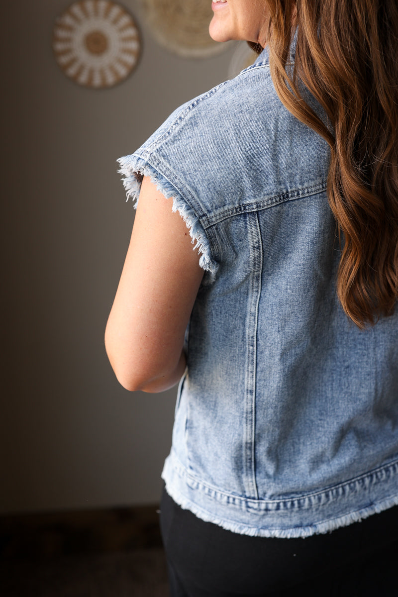 Person wearing a denim vest with a neutral background