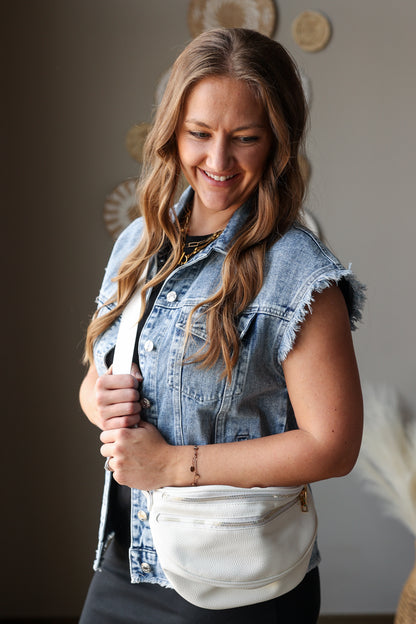 Woman wearing a denim vest over a black midi dress, holding a white bag.