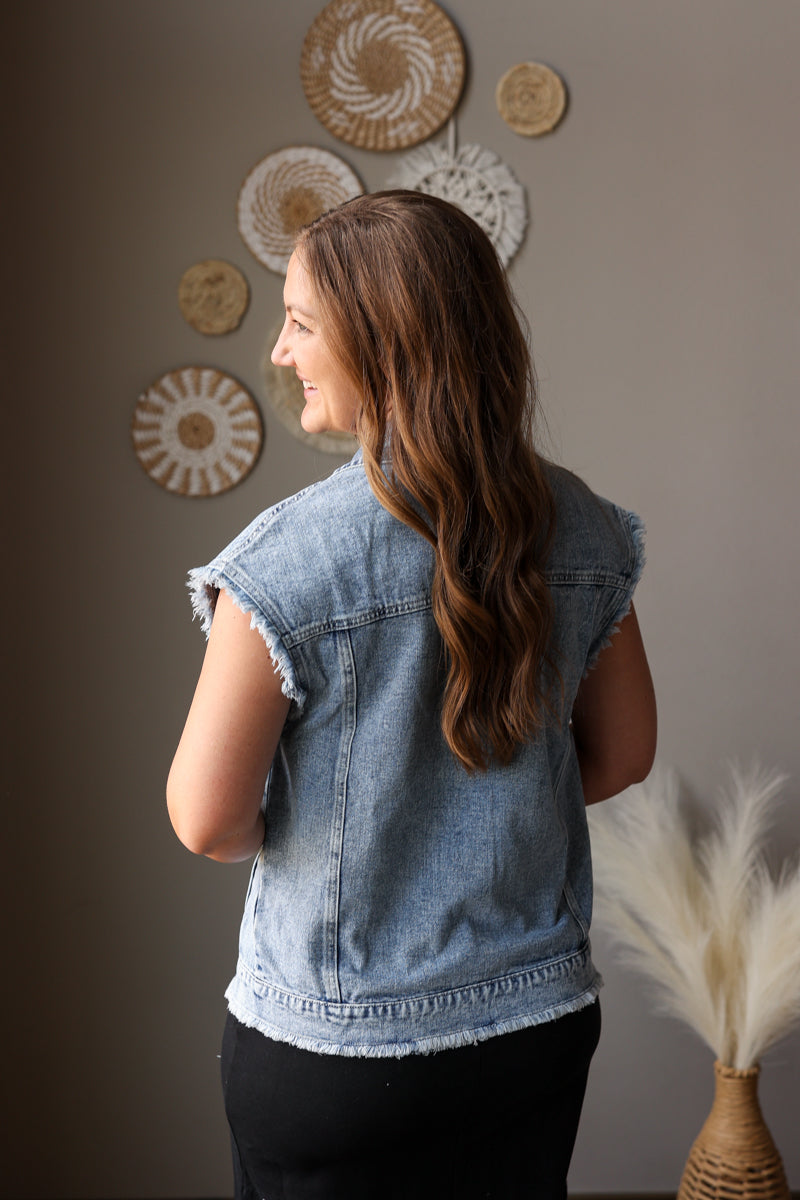 Woman wearing a denim vest standing against a wall with decorative plates.