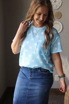 Woman wearing a light blue polka dot shirt and blue jean skirt indoors.