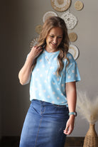 Woman wearing a light blue top with white polka dots and a denim skirt, standing indoors.
