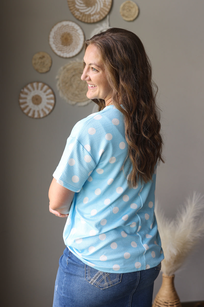 Woman wearing a light blue polka dot shirt in a room with decorative wall art.