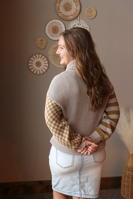 Woman wearing a patterned sweater and denim skirt standing against a wall with decorative plates.