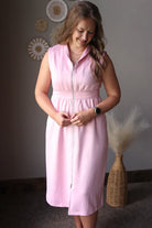 Woman wearing a pink dress standing against a neutral wall with decorative elements.