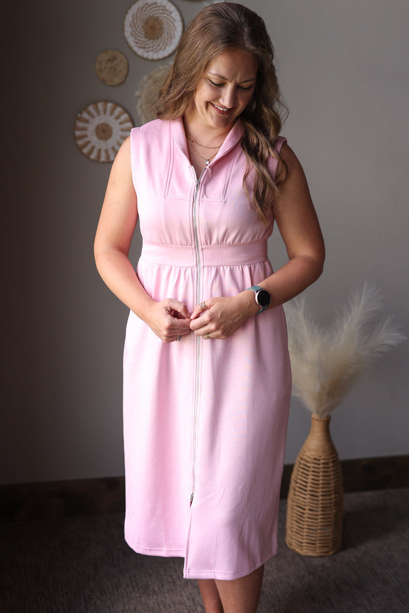 Woman wearing a pink dress standing against a neutral wall with decorative elements.
