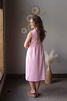 Woman in a pink dress standing in a room with decorative wall art and a vase.