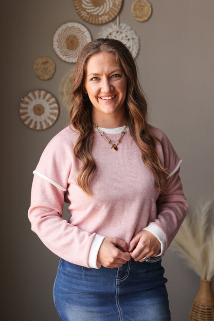 Woman wearing a pink sweater and blue jeans standing in front of decorative wall art.