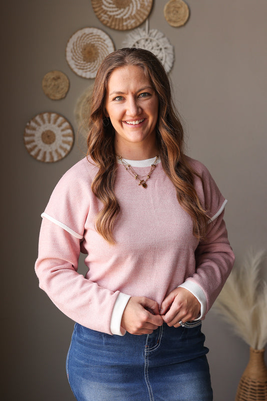 Woman wearing a pink sweater and blue jeans standing in front of decorative wall art.