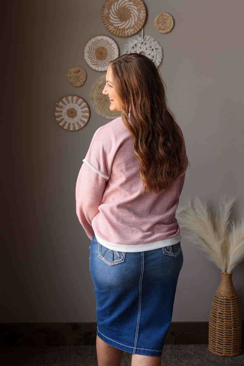 Woman wearing a pink sweater and blue denim skirt standing in a room with decorative plates on the wall.