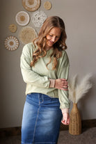 Woman wearing a light green sweater and blue skirt standing in a room with decorative wall hangings.
